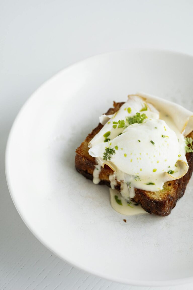 A delicious gourmet toast topped with poached egg and creamy sauce on a white plate.