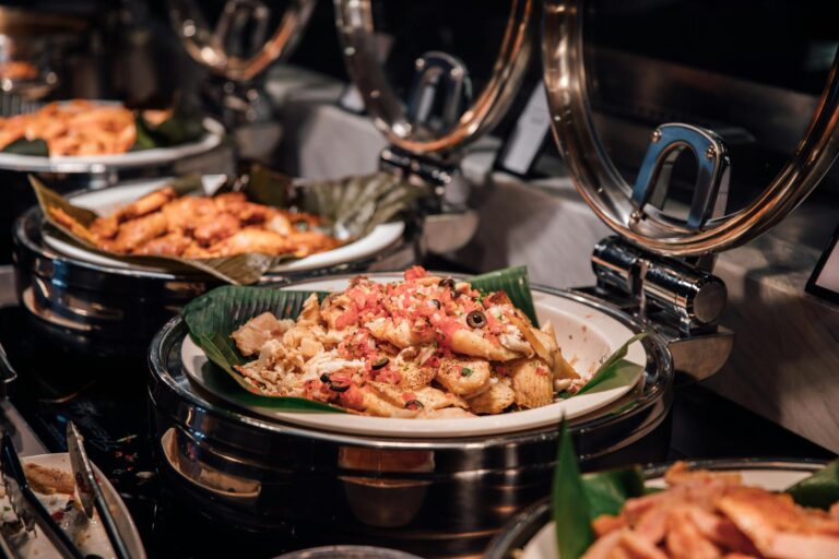 Close-up of appetizing pasta dishes at an elegant buffet with warm lighting and garnishes.