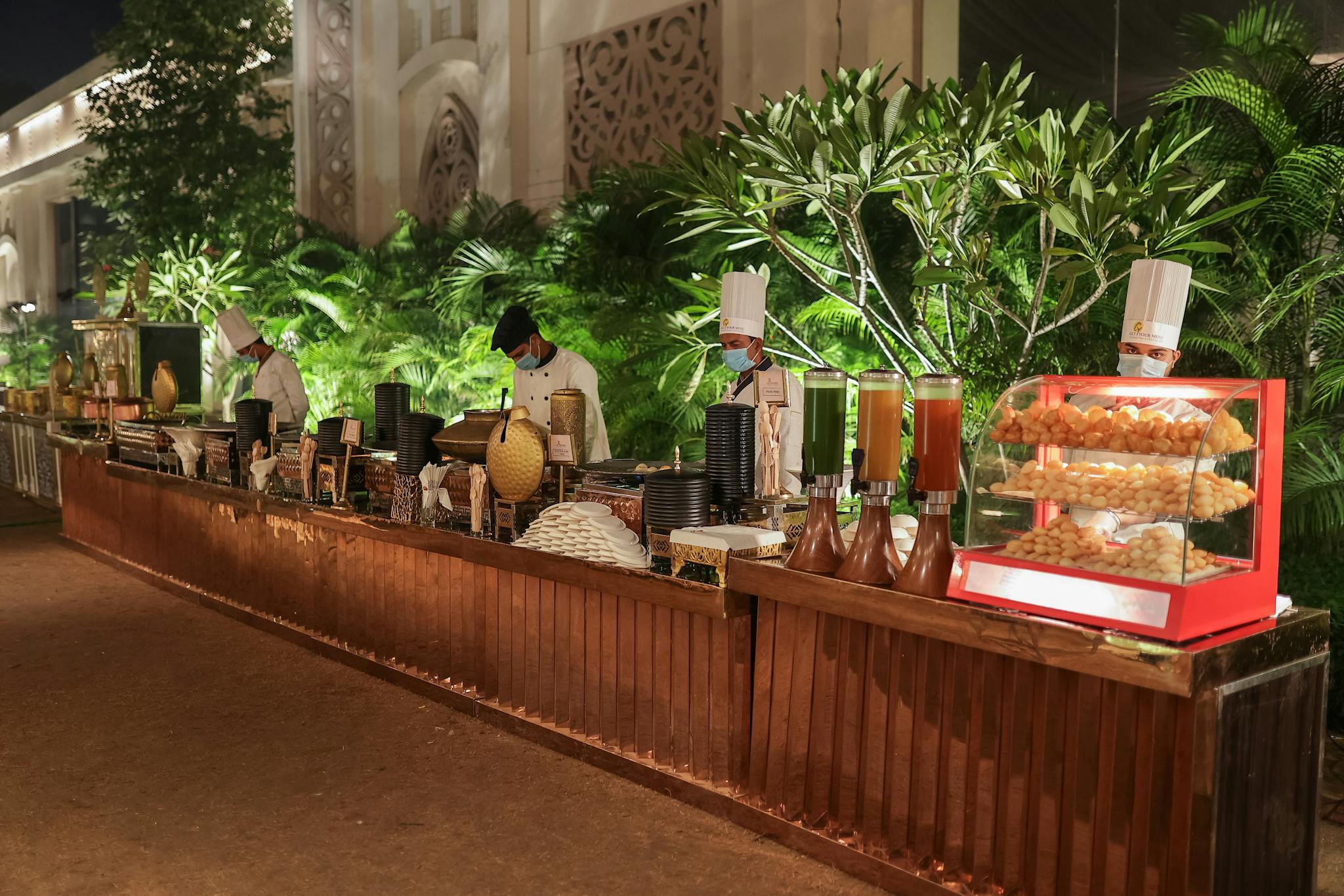 Elegant outdoor buffet setup at night with chefs preparing food. Ideal for event themes.