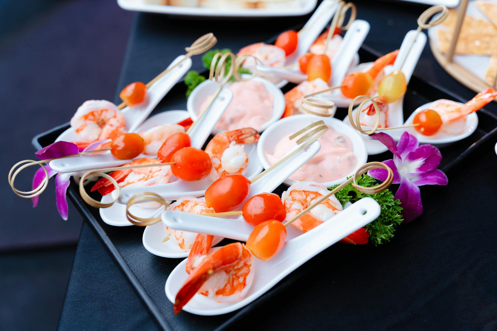 Tasteful shrimp and cherry tomato appetizers with sauce, adorned with flowers on a white spoon.